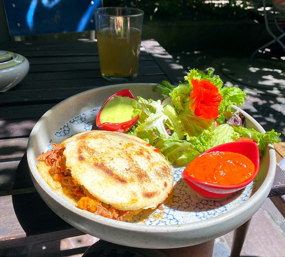 Arepa Reina Pepiada mit Salat und zwei Dips auf einem Tisch in der Sonne