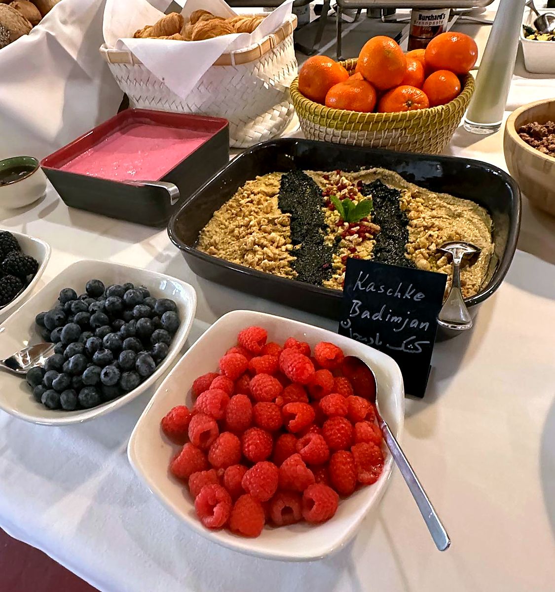 Schalen mit Himbeeren und Heidelbeeren, dahinter Mandarinen und ein Auflauf