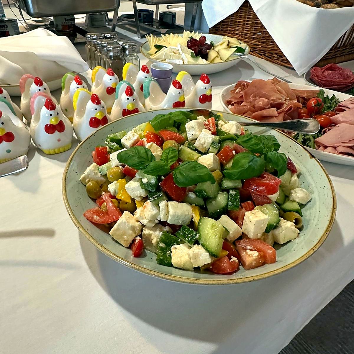 Großer Salat mit Feta, Gurke und Tomaten, daneben Eierbecher in Hühnchenform und Aufschnitt