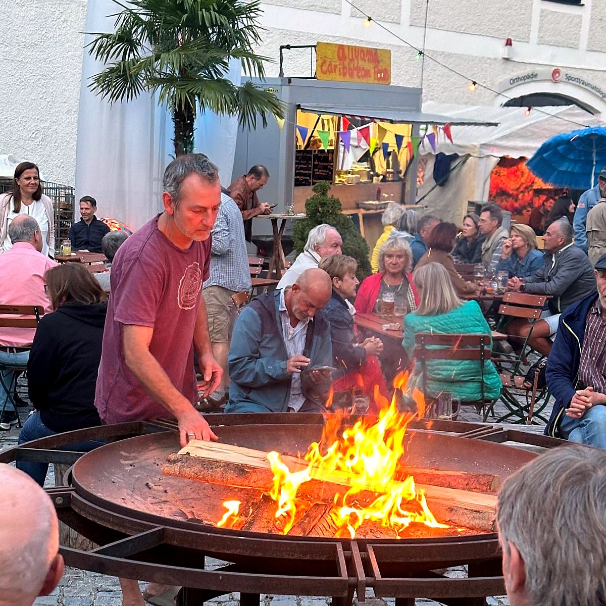 Der Stand von Auyama Caribbean Food bei einem Fest im Freien, vorne lodert eine Feuerschale, rundherum feiern Gäste an Biertischen